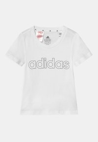 Bílý dětský tričko s krátkým rukávem s velkým nápisem "adidas" tištěným v obrysu přes hruď, velikostní štítek viditelný uvnitř límce.