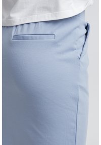 Ljusblå byxor med en mjuk yta, med en dold bakficka och en avslappnad passform. Tyget är mjukt och stretchar.