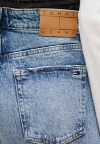 Τσέπη παντελονιού από ανοιχτό μπλε τζιν με μικρό λογότυπο Tommy Hilfiger και καφέ δερμάτινο ταμπελάκι με την ένδειξη "Tommy Jeans" στη μέση της μέσης.