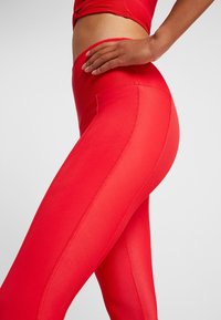 Czerwone legginsy z żeberkową strukturą, wysokim pasem i eleganckim fasonem. Detale po stronie szwu dodają ubraniu zorganizowanego wyglądu.