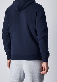 Sudadera azul marino con capucha, con puños y dobladillo acanalados. Combinada con pantalones jogger gris claro, que presentan un diseño simple y casual.