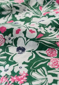 Tkanina s cvetnim vzorom na zeleni podlagi, ki vsebuje bele cvetove, rožnate detajle in zapleteno oblikovane liste z mehkimi teksturami.