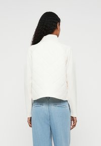 Casaco branco acolchoado com colarinho alto e mangas raglan, combinado com jeans azul claro. Tecido macio com um corte cropped.