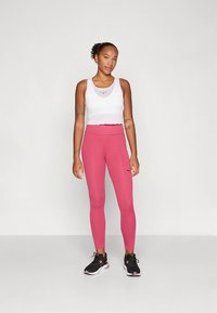 Rózsaszín magas derekú leggings, fehér rövidített toppal párosítva. A leggings sima textúrájú, apró logóval díszítve.