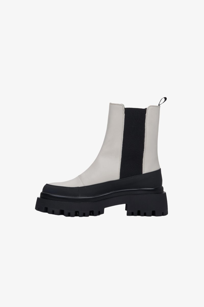 Bílé kožené kotníkové boty s černým elastickým panelem, robustní černou podrážkou a poutkem. Mají hladký povrch a výrazný vzor na podrážce.