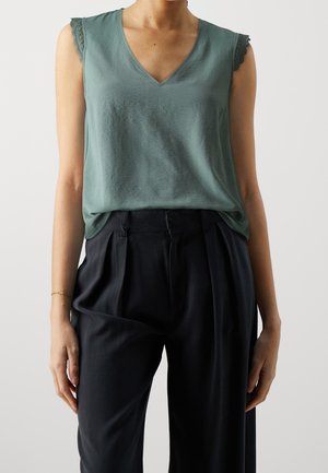 Haut sans manches vert avec un col en V et des accents en dentelle sur les épaules, associé à un pantalon sombre taille haute. Texture lisse, coupe décontractée.