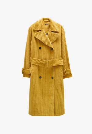 Musztardowo-żółty, prążkowany kordowy płaszcz dwurzędowy z paskiem w talii, dużymi klapami i zapiętymi mankietami. Posiada dwie przednie kieszenie.
