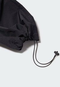 Ourlet ajustable noir avec un cordon de serrage et un piton. Le tissu est lisse, et le design présente des détails froncés pour un look ajusté.