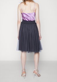 Camisole in raso viola con sottili spalline abbinata a una gonna in tulle nero con vita arricciata e motivo a pois. Sandali trasparenti con tacco.