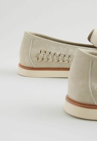 Scarpe in suede beige con un design intrecciato sul lato, suola in gomma con un accento marrone chiaro e punta arrotondata.