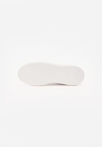 Bílá podrážka tenisky s texturovaným vzorem pro trakci, hladkými okraji a značkovým detailem. Čistý design, lehký vzhled, minimalistický styl.