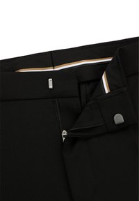 Black trousers featuring a zipper and button closure, with a smooth texture. Inside waistband has gold and white stripes as accents.