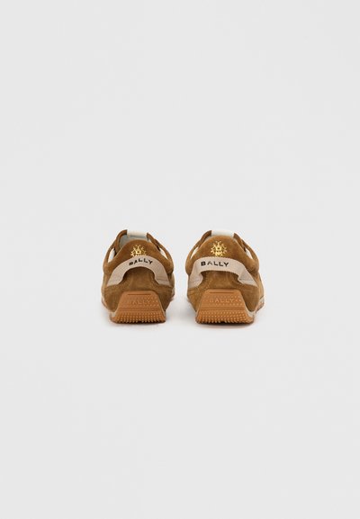 Sneakers de camurça castanha com detalhes em bege, apresentando uma sola de borracha texturizada e detalhe do logotipo no calcanhar e na língua. Vista em ângulo traseiro.