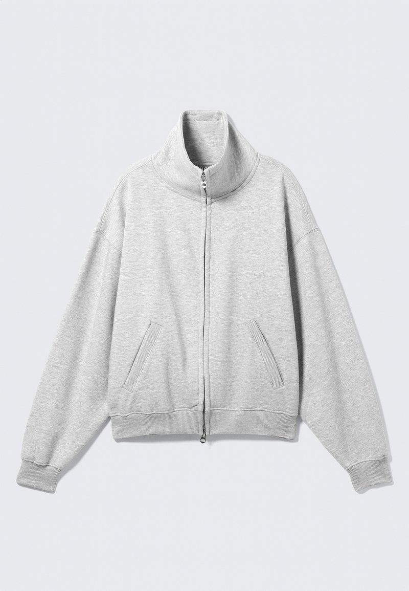 Sweat-shirt gris clair à fermeture éclair avec col haut, poches latérales et poignets côtelés. Confectionné dans un tissu doux avec une coupe décontractée et un design légèrement oversize.