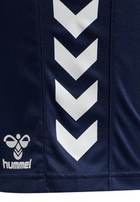 Navy sports jersey featuring large white chevron patterns on the side and a small white logo at the lower left, made of smooth fabric.