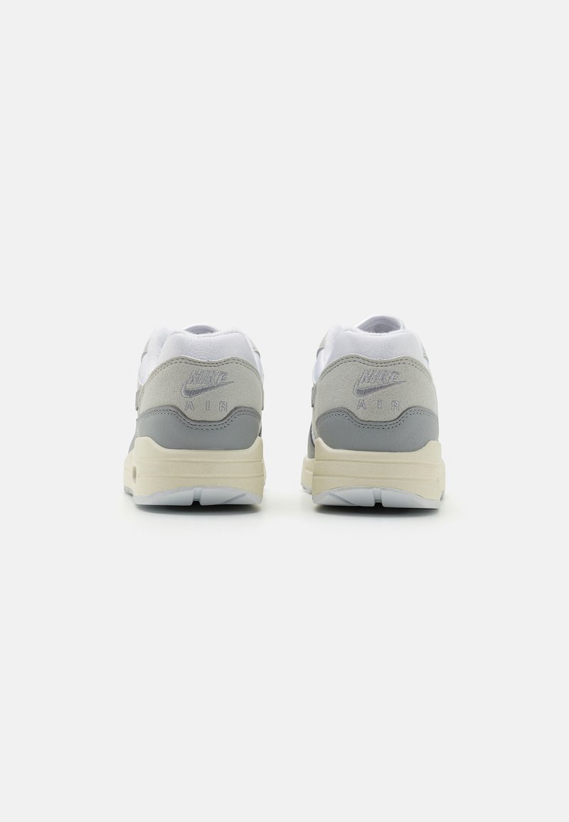 Grijze en witte sneakers met een bovenwerk van suede, gestructureerde meshpanelen, gewatteerde kraag en een crèmekleurige tussenzool. Nike-logo op de hiel.