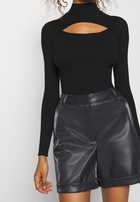 Czarna, prążkowana bluzka z długim rękawem, stójką i wycięciem, zestawiona z czarnymi, wysokim stanem, błyszczącymi szortami z ekologicznej skóry.