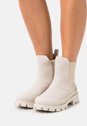 Botas de tobillo beige de tela texturizada con una suela de goma resistente, que cuentan con un cierre lateral y una lengüeta en la parte posterior.