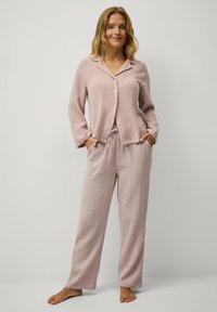 Lichtroze twee-delige pyjama set van gestructureerde stof. Het topje heeft een kraag, knoopsluiting en lange mouwen. De broek heeft een losse pasvorm.