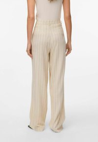 Wijdere broek in crème met verticale streepjes. Heeft een hoge tailleband en twee achterzakken. Zachte textuur met een vloeiende silhoutte.