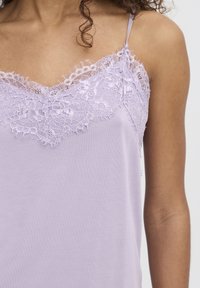 Lavandas krūšturis ar smalku mežģīņu apdari ap kaklu, ar tievām regulējamām siksnām un gludu, vieglu audumu.