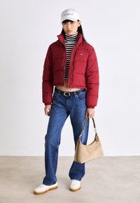 Röd puffjacka med elastiska mudd, svart och vit randig polotröja, blå jeans, vita sneakers och beige handväska med axelrem.