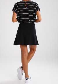 Svart kjol med utsvängd design, i kombination med en kortärmad svart och vit randig topp. Vita sneakers med svarta detaljer fulländar outfiten.