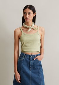 Light green ribbed tank top with square neckline, paired with a high-waisted denim skirt. The model wears a light patterned scarf around the neck.