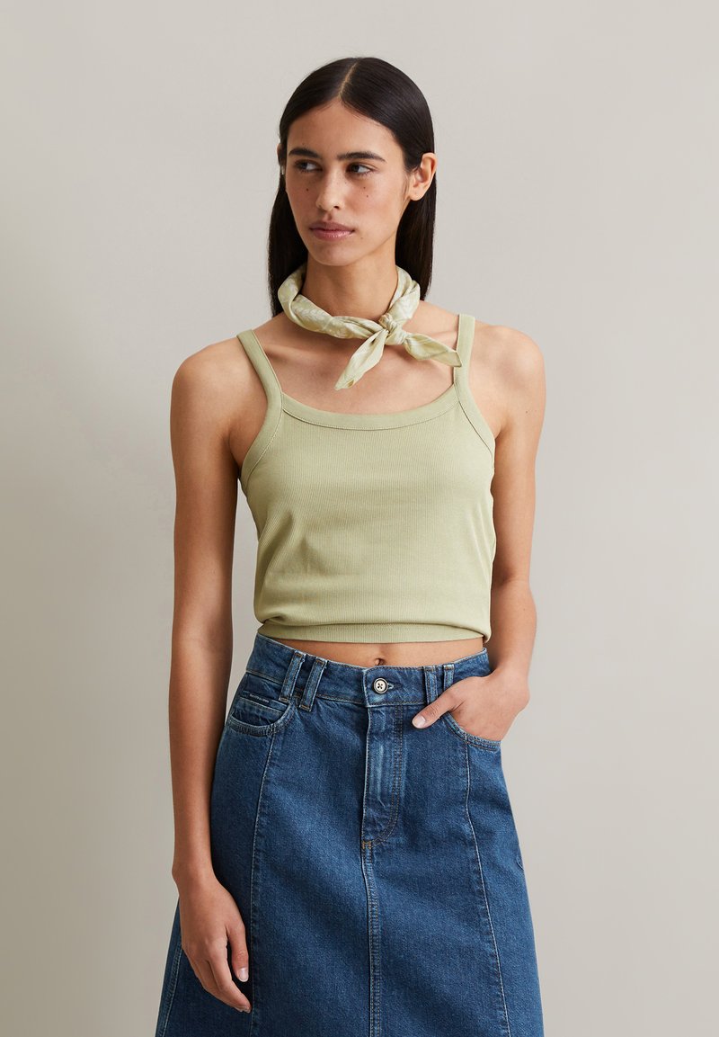 Light green ribbed tank top with square neckline, paired with a high-waisted denim skirt. The model wears a light patterned scarf around the neck.