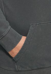 Donkergrijze katoenen hoodie met een gestructureerde afwerking, ribbelmanchetten en een voorkantzak. Zichtbare stikseldetails benadrukken het ontwerp.