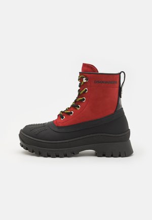 Red and black hiking boots featuring a suede upper, rubber lower, metal eyelets, and thick cleated soles for enhanced grip.