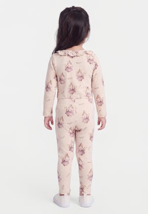 Barn med langt mørkt hår iført lyserød pyjamas med egern i kjoler, stående med ryggen mod en ensfarvet hvid baggrund.