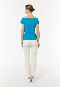 Turkusowa bluzka bez ramiączek z krótkimi rękawami, zestawiona z białymi dopasowanymi spodniami i jasnobrązowymi szpilkami, widziana z tyłu.