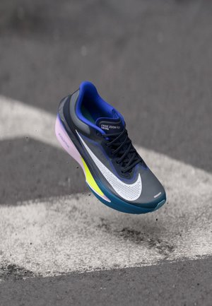 Chaussure de course Nike Zoom Fly gris foncé avec swoosh blanc, semelle bleu et jaune néon, flottant au-dessus de l'asphalte avec des marquages routiers blancs.