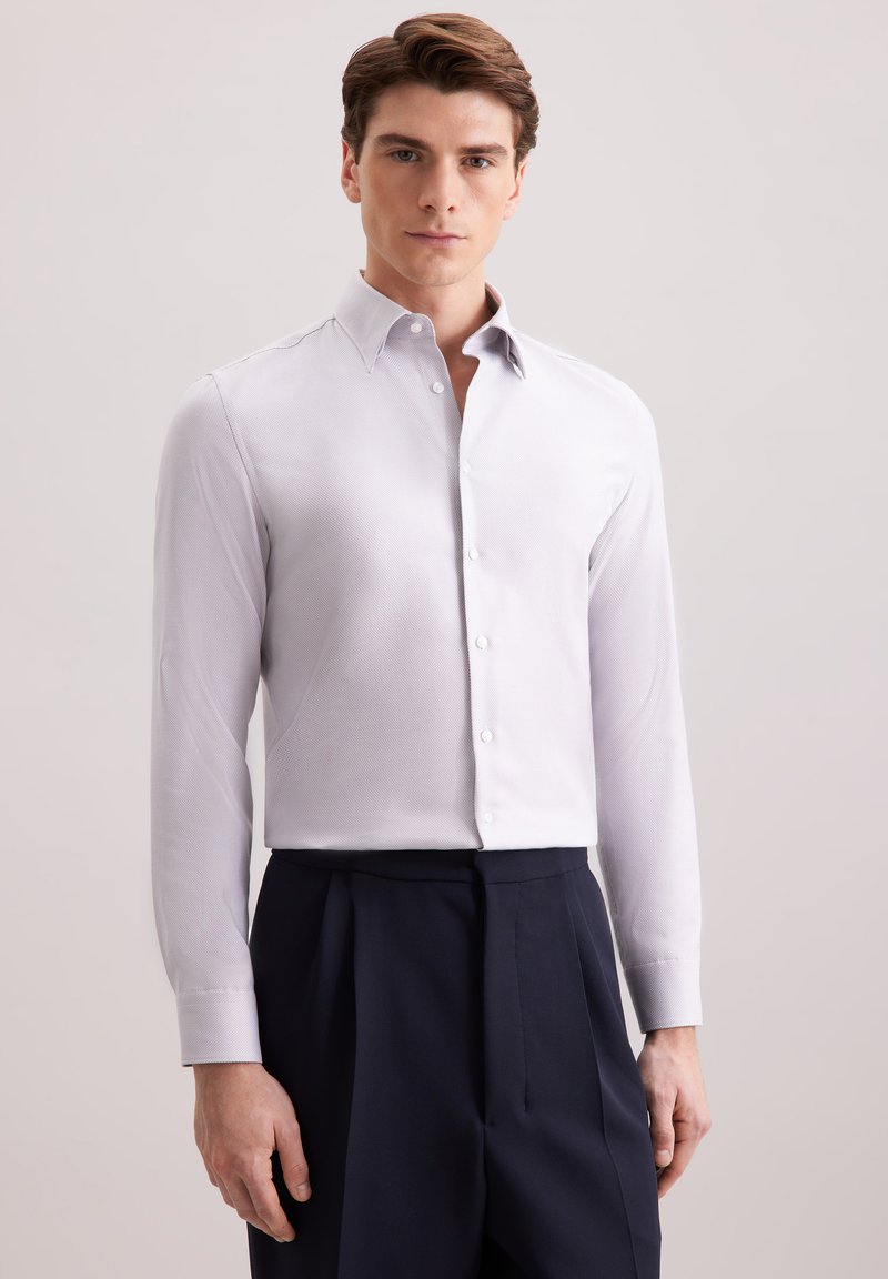 Chemise à manches longues gris clair avec col et boutons blancs, présentant une texture subtile, portée avec un pantalon bleu marine foncé.