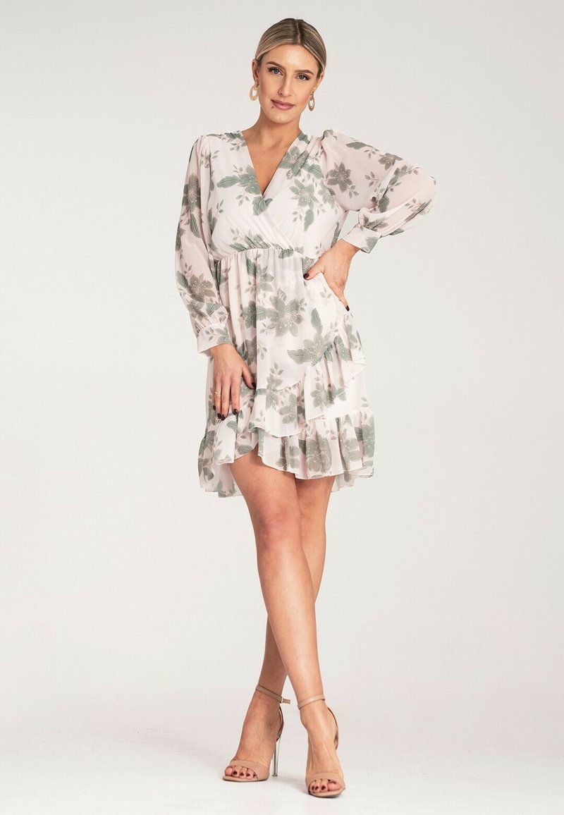 Kwiatowa sukienka zapinana z przodu w jasnoróżowym kolorze z zielonymi wzorami liści, z długimi rękawami i falbaniastym dołem. Posiada dopasowaną talię oraz miękką, zwiewną tkaninę.