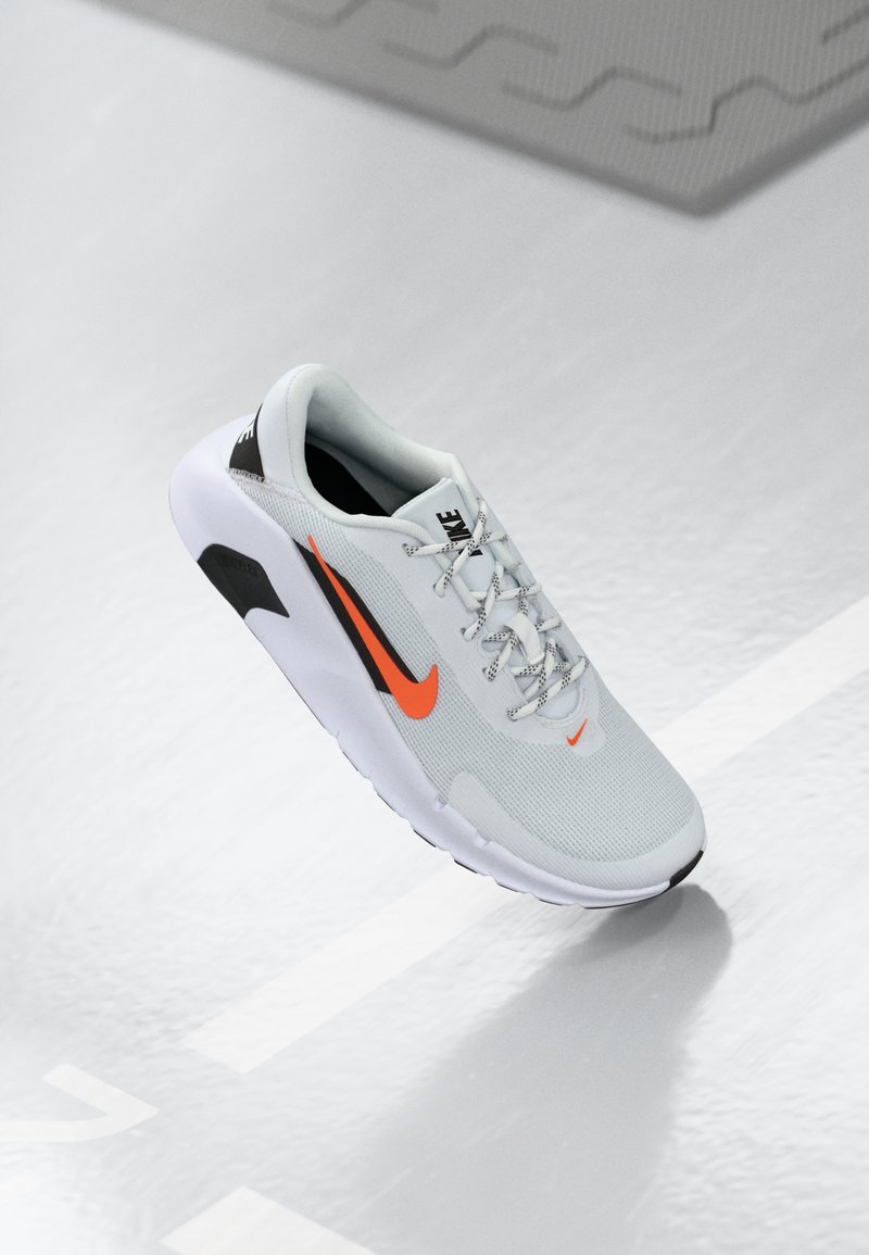 Nike sportsko i lys grå mesh med orange detaljer. Har rund tå, snørebåndsdesign, polstret sål og sorte hæl- og ydersålsdetaljer.