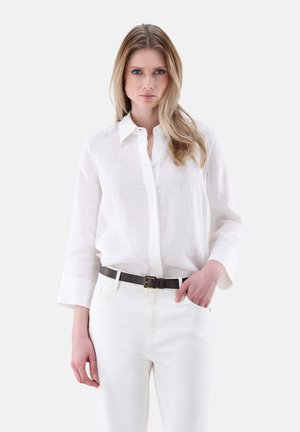 Camicia bianca in lino con bottoni e maniche lunghe, abbinata a pantaloni bianchi e una cintura in pelle marrone scuro con fibbia dorata.