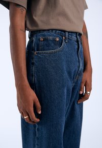 Jeans in denim blu scuro con vestibilità dritta, caratterizzati da rivetti in rame, design a cinque tasche e una sottile trama.