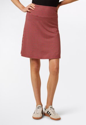 Roter Rock mit Muster, tailliert und leicht ausgestellt. Das Muster besteht aus kleinen weißen und schwarzen Formen und ist aus einem glatten Stoff gefertigt.