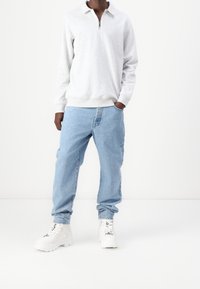 Sudadera gris con cremallera, jeans de mezclilla azul claro y zapatillas gruesas blancas. Incluye características como cuello, puños acanalados y bolsillos laterales.