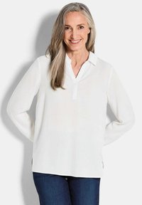 Witte blouse met lange mouwen en een V-hals, met knopenrij, gemaakt van lichtgewicht stof; gecombineerd met donkerblauwe jeans. Soepele textuur.