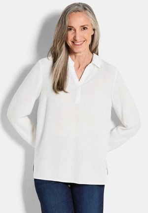 Witte blouse met lange mouwen en een V-hals, met knopenrij, gemaakt van lichtgewicht stof; gecombineerd met donkerblauwe jeans. Soepele textuur.