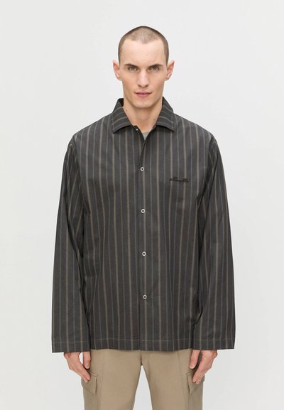 Chemise à rayures noires à manches longues avec col, fermeture à boutons et logo sur la poitrine. Le tissu a une texture lisse et une coupe décontractée.