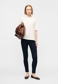 Μπεζ υπερμεγέθη μπλουζάκι, σκούρα στενά τζιν, καφέ δερμάτινη τσάντα, καφέ φλατ παπούτσια. Απλός σχεδιασμός, ομαλή υφή, καθημερινή εμφάνιση.