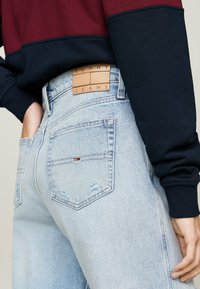 Heledad sinine teksapüksid, millel on regulaarne lõige, sisaldavad nahklabelit, millel on kirjas "TOMMY JEANS" ja väike logotagi tagaosal.