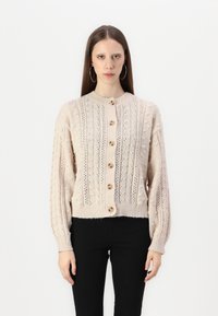 Cárdigan de punto color crema con cuello redondo, patrones texturizados y botones de madera en la parte delantera; mangas largas y abullonadas que se ajustan en los puños.