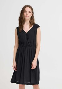 Rochie neagră fără mâneci, cu decolteu în V, detalii pliate la umeri și talie elasticizată. Siluetă în forma literei A, fabricată dintr-un material texturat.