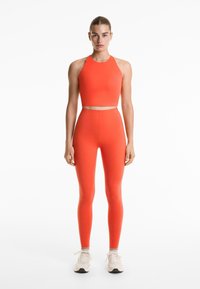 Twee-delig sportoutfit in fel oranje; bestaat uit een nauwsluitende crop top met een hoge halslijn en high-waisted leggings met een zachte textuur.