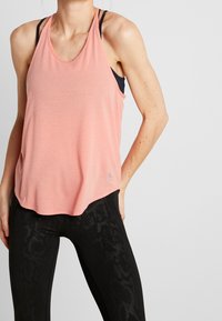 Světlounce růžový sportovní top s výstřihem do oblouku, kombinovaný s černými legínami s jemným hadím vzorem.